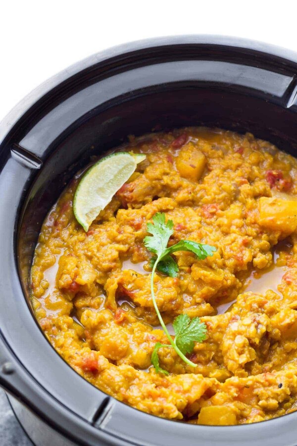 Overhead shot of butternut squash lentil curry in the slow cooker with fresh lime wedge and cilantro