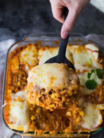 close up shot of cauliflower rice chicken enchilada casserole with a hand serving a spoonful