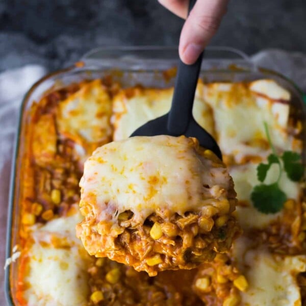 close up shot of cauliflower rice chicken enchilada casserole with a hand serving a spoonful