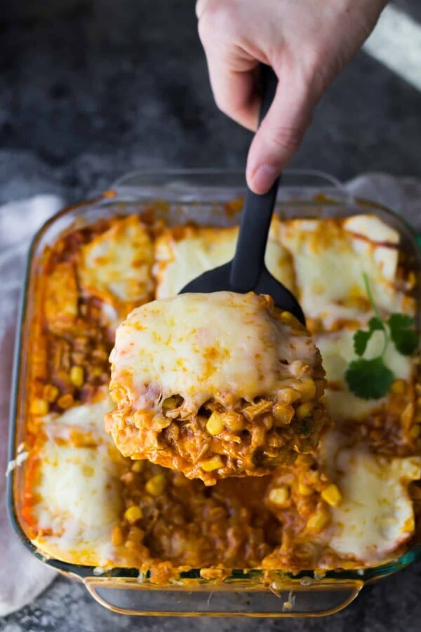 close up shot of cauliflower rice chicken enchilada casserole with a hand serving a spoonful