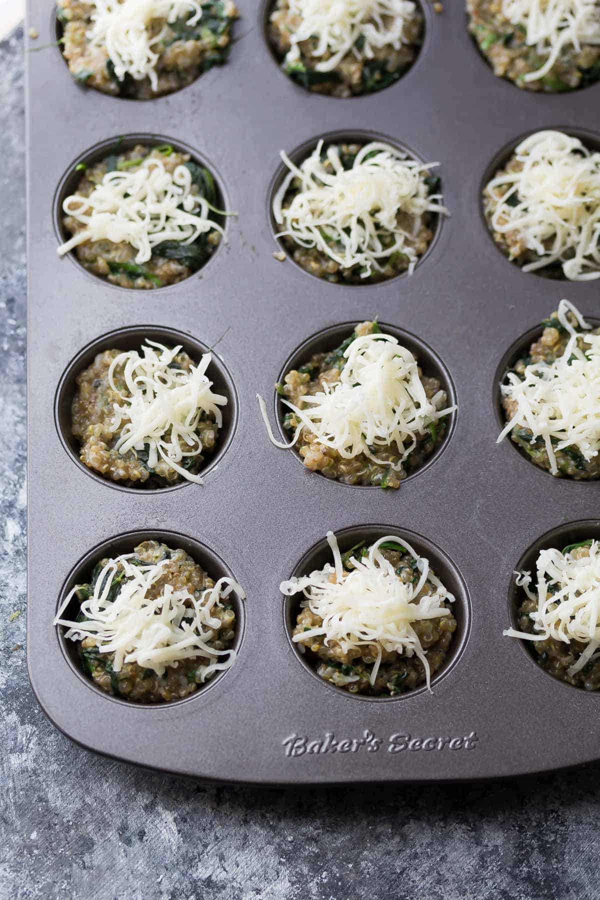 Cheesy Spinach Quinoa Cups mixture in muffin baking tin with shredded cheese on top before baking