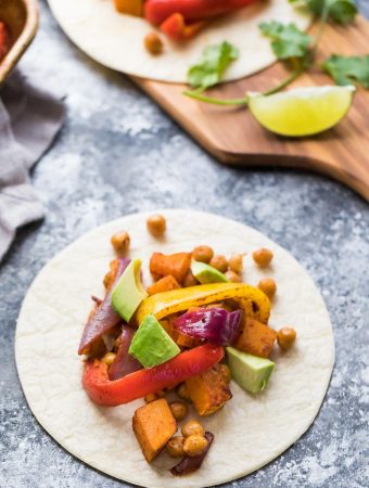 white plate with chickpea butternut squash fajitas on gray counter with fresh avocado and lime