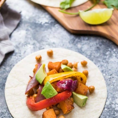 white plate with chickpea butternut squash fajitas on gray counter with fresh avocado and lime