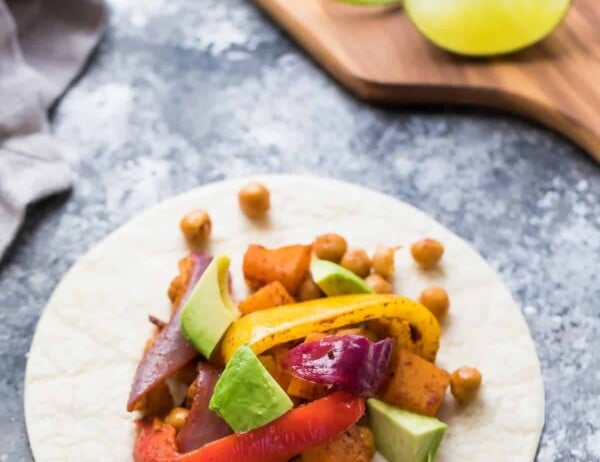 white plate with chickpea butternut squash fajitas on gray counter with fresh avocado and lime