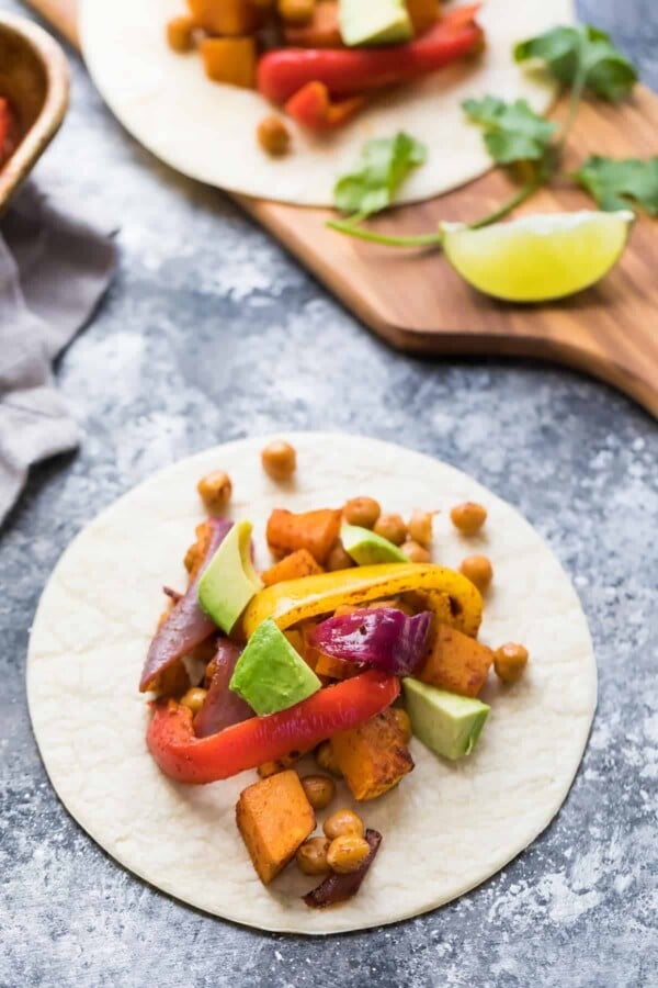 white plate with chickpea butternut squash fajitas on gray counter with fresh avocado and lime