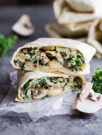 breakfast burrito with kale and mushrooms cut i half on parchment with fresh kale next to it