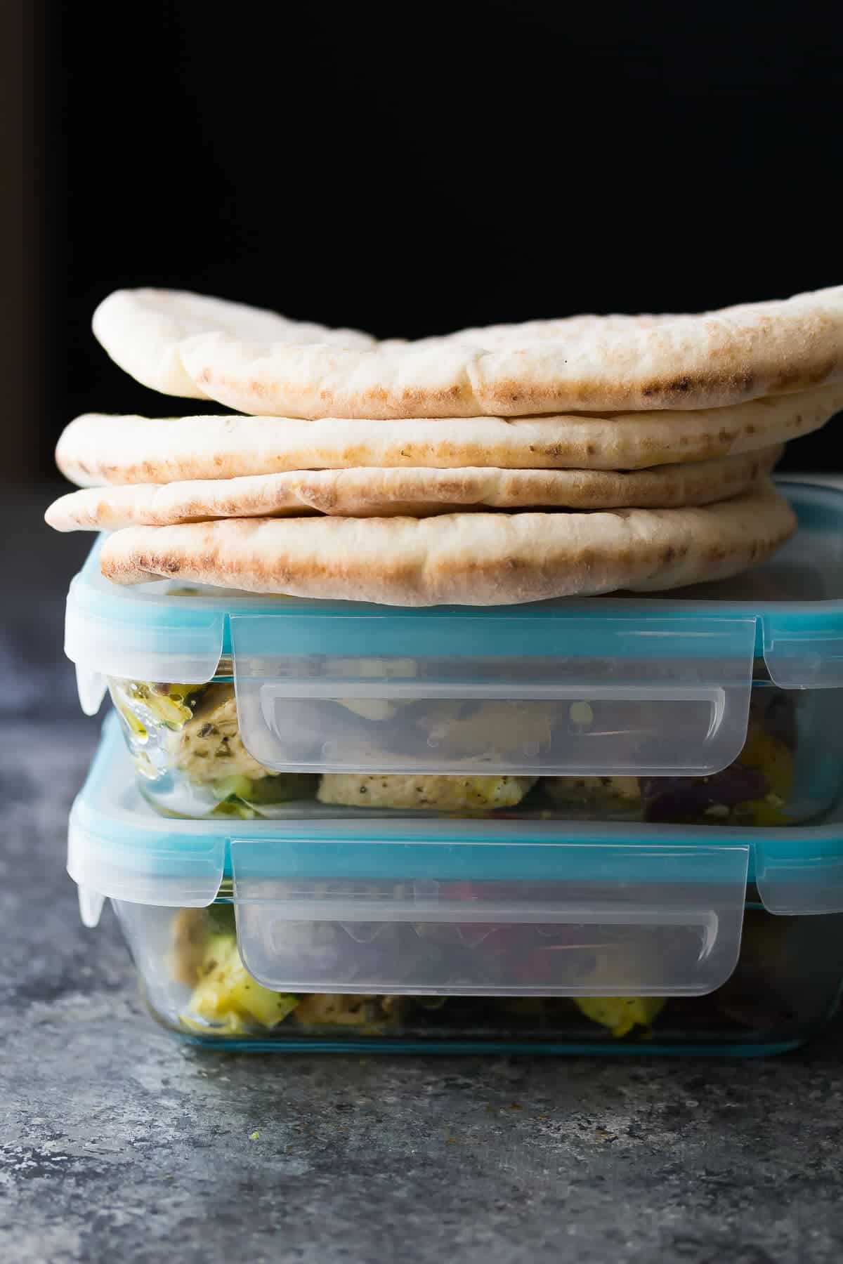 pesto chicken and vegetables in meal prep containers with pitas on top