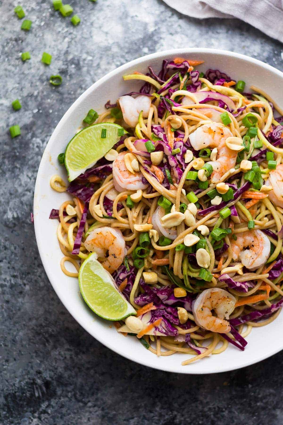 overhead shot of spiralized veggie thai noodle bowl in large white bowl with fresh limes