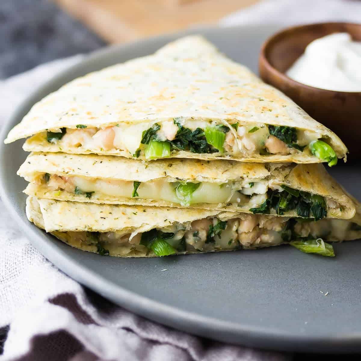 Stack of three Smashed White Bean and Spinach Quesadillas on gray plate with side of yogurt