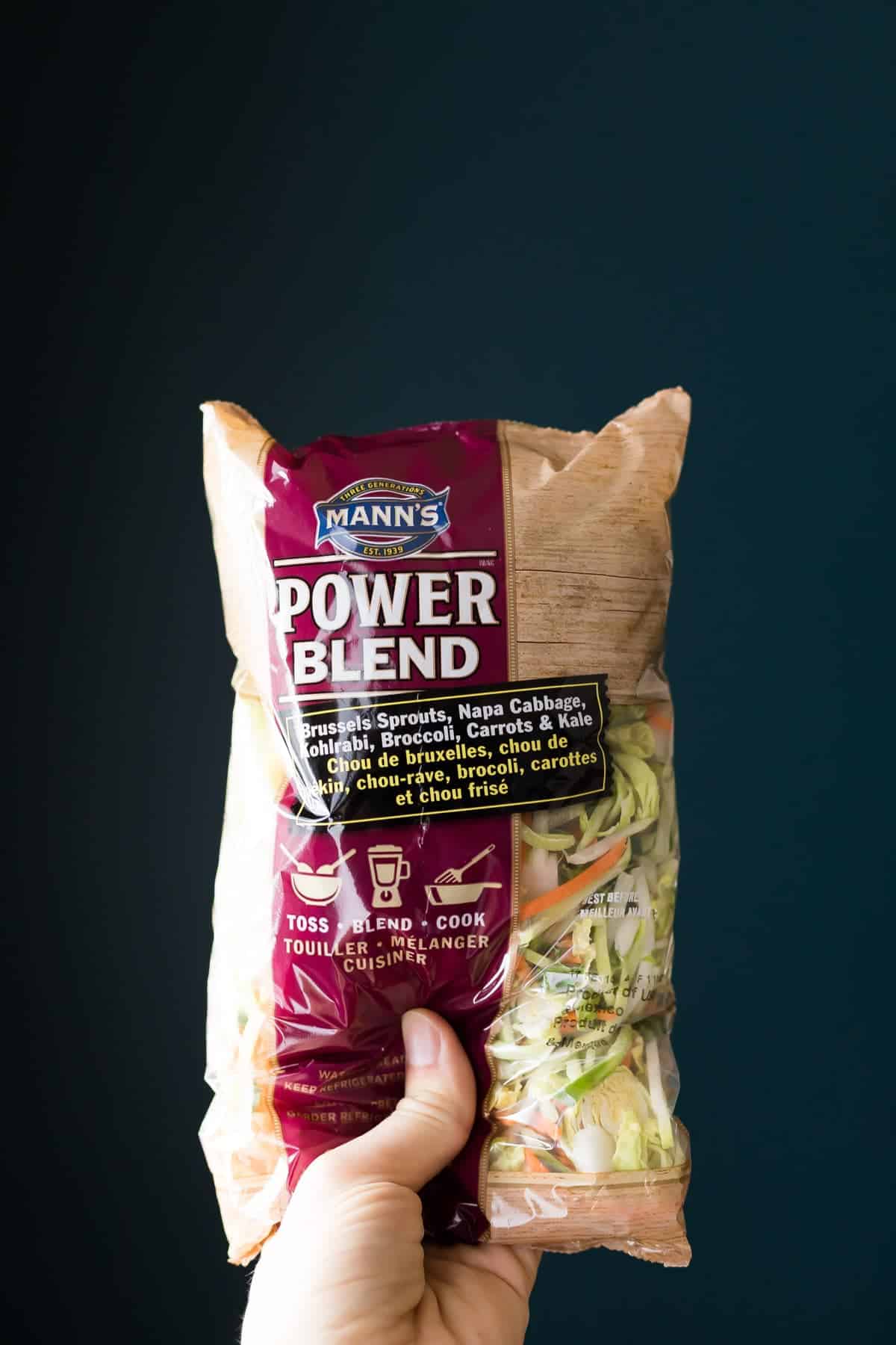 Hand holding up a bag of Mann's Power Blend salad mix