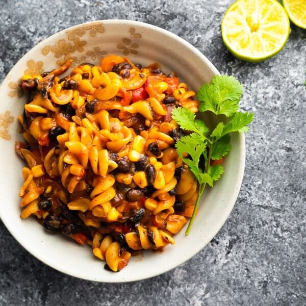 overhead shot of black bean fajita pasta in white bowl with parsley sprig and limes