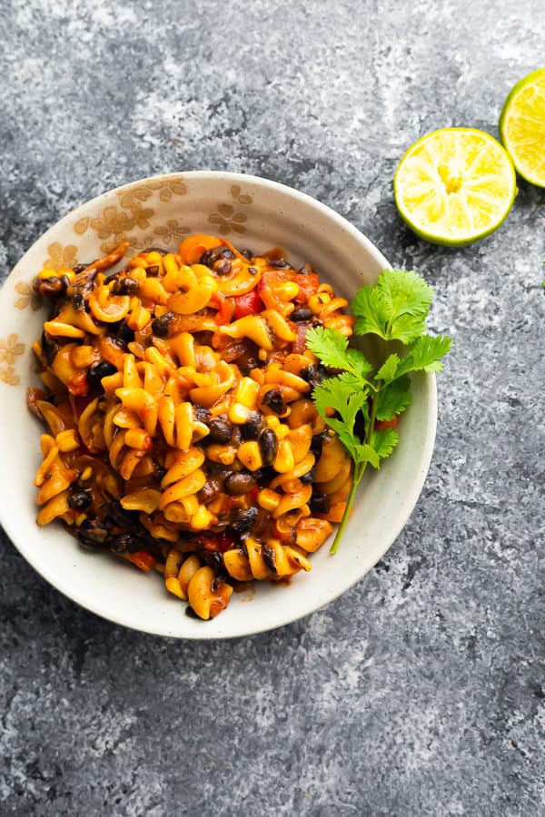 overhead shot of black bean fajita pasta in white bowl with parsley sprig and limes