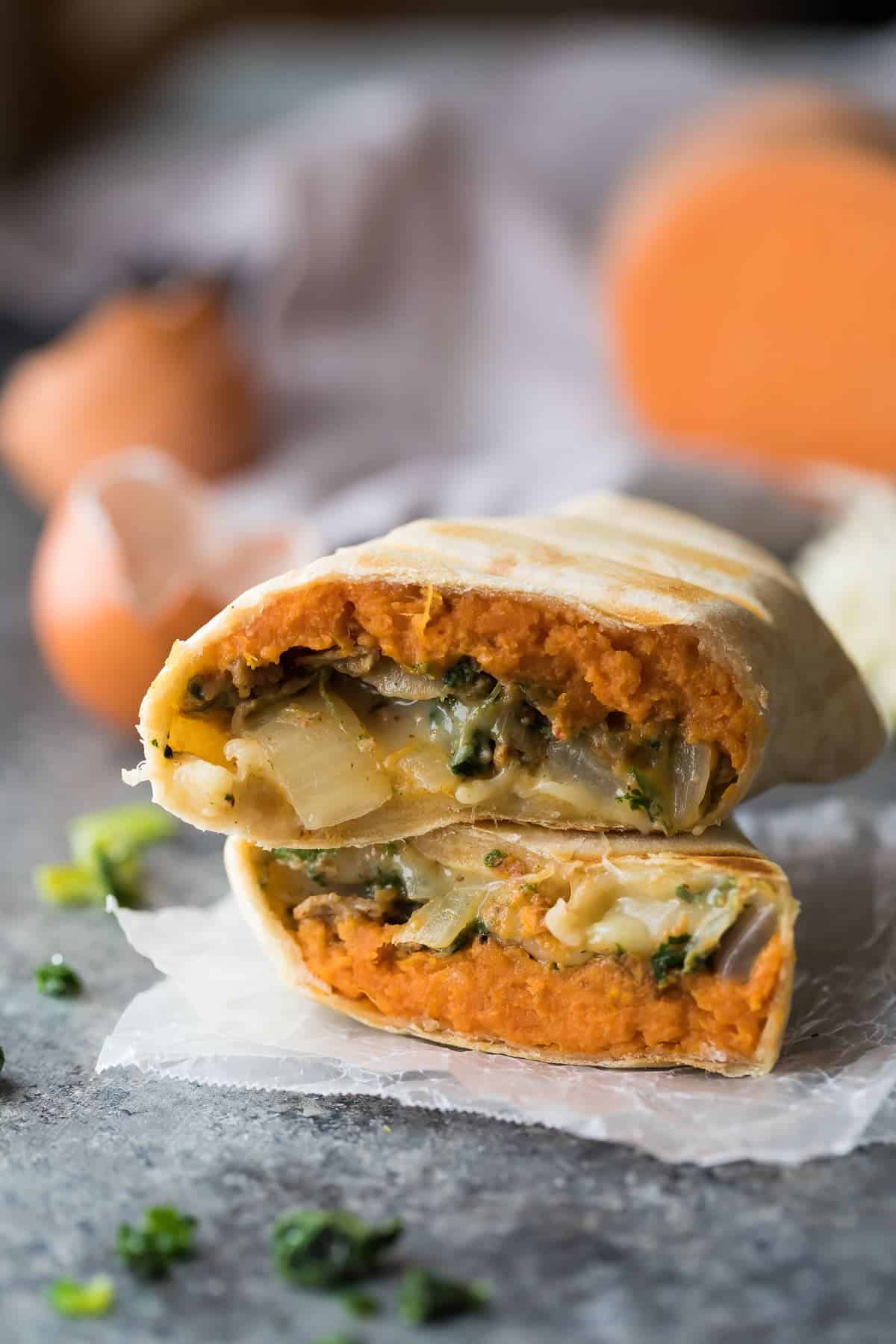 close up view of a southwestern sweet potato breakfast burrito cut in half stacked on parchment paper