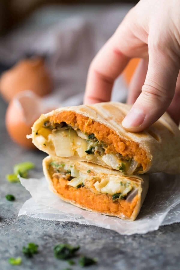 hand holding a sweet potato breakfast burrito cut in half on parchment