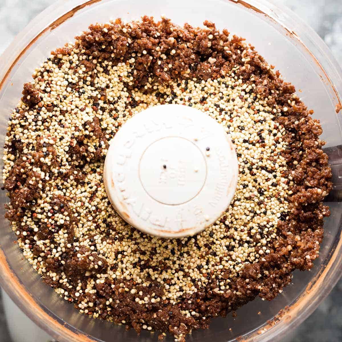 overhead view of ingredients for Chocolate Almond Quinoa bars in the food processor with toasted quinoa added