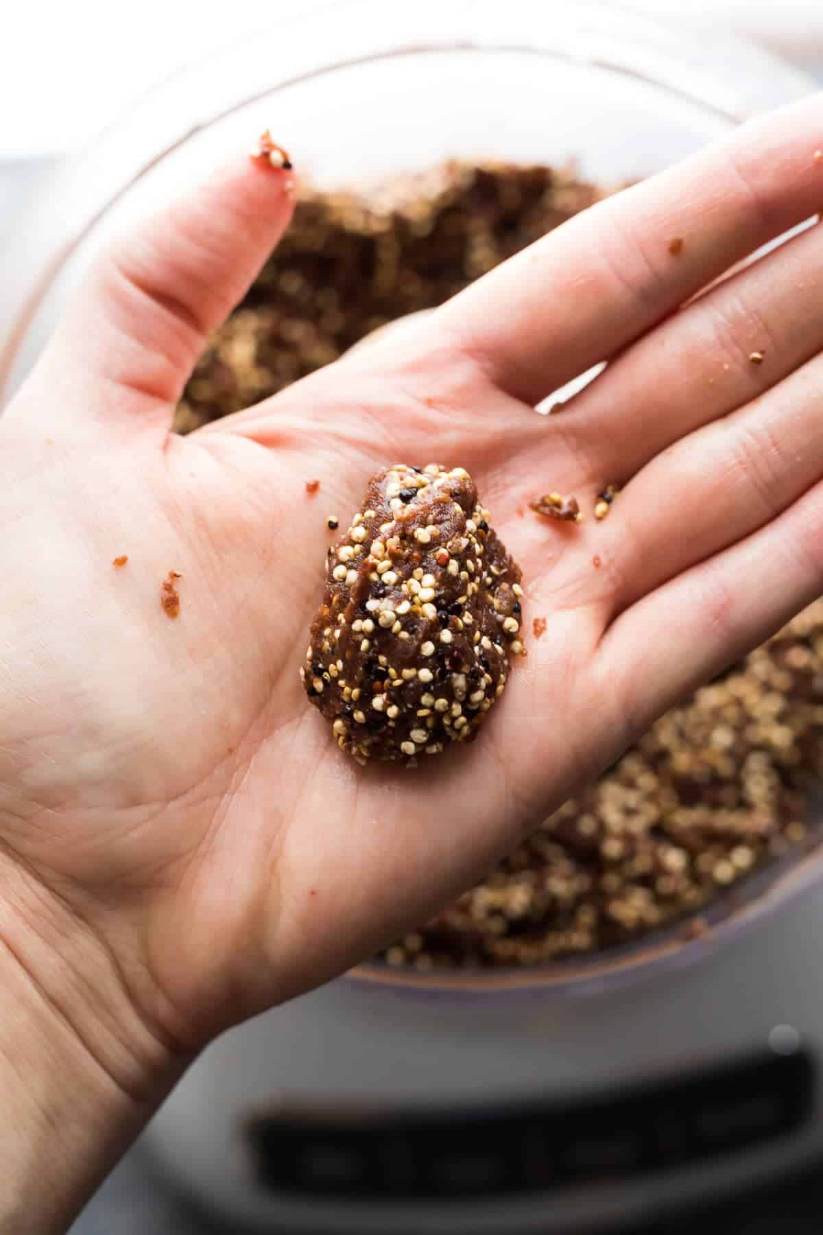 a hand with a ball of the mixture for Chocolate Almond Quinoa bars 