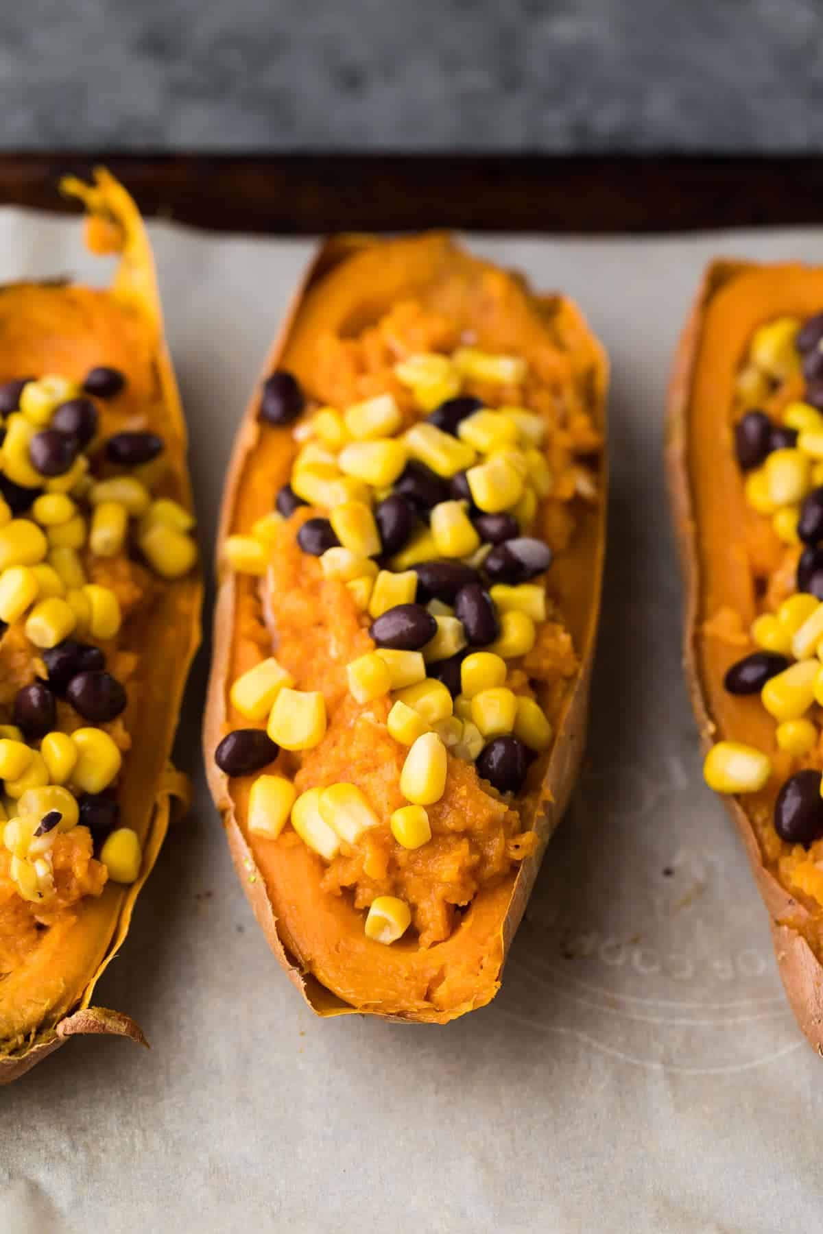 Halved Sweet Potatoes lined up on a baking sheet with stuffing in the middle