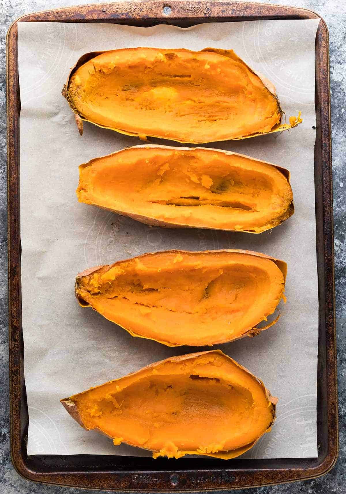 overhead view of four halved sweet potatoes on a lined baking sheet