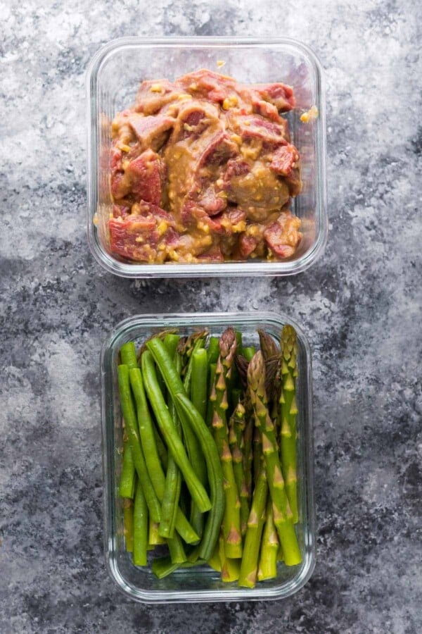 Overhead view of two glass containers filled with raw hoisin ginger steak and cut green beans and asparagus