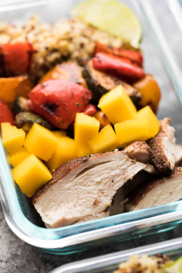 close up view of jerk chicken mango and roasted vegetables in glass container