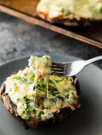 lasagna stuffed portobello mushroom on gray plate with fork taking a bite