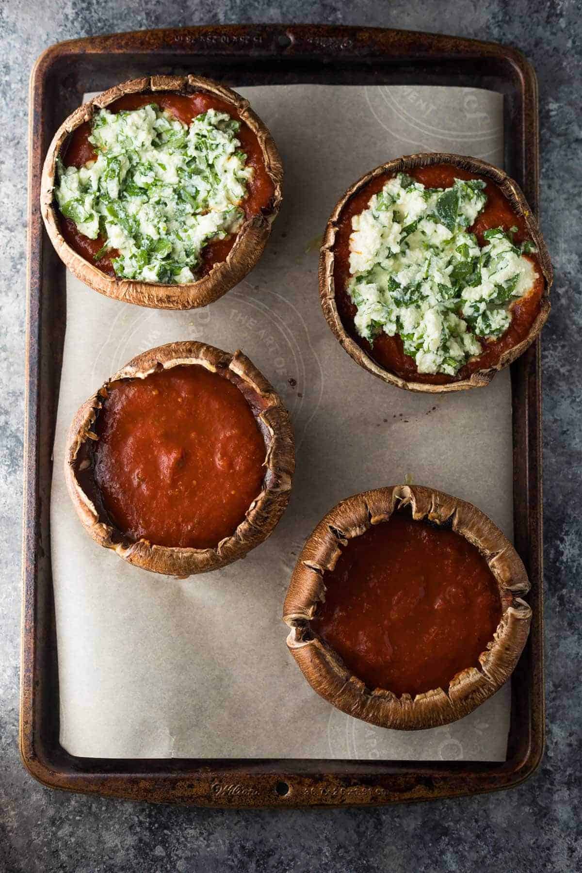 four portobello mushroom caps stuffed with tomato sauce and toppings on baking tray