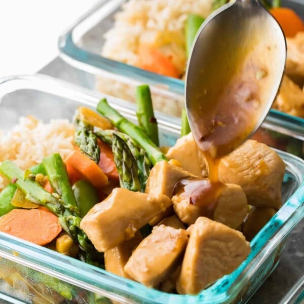 glass meal prep container with maple ginger chicken bowl and spoon drizzling the dressing