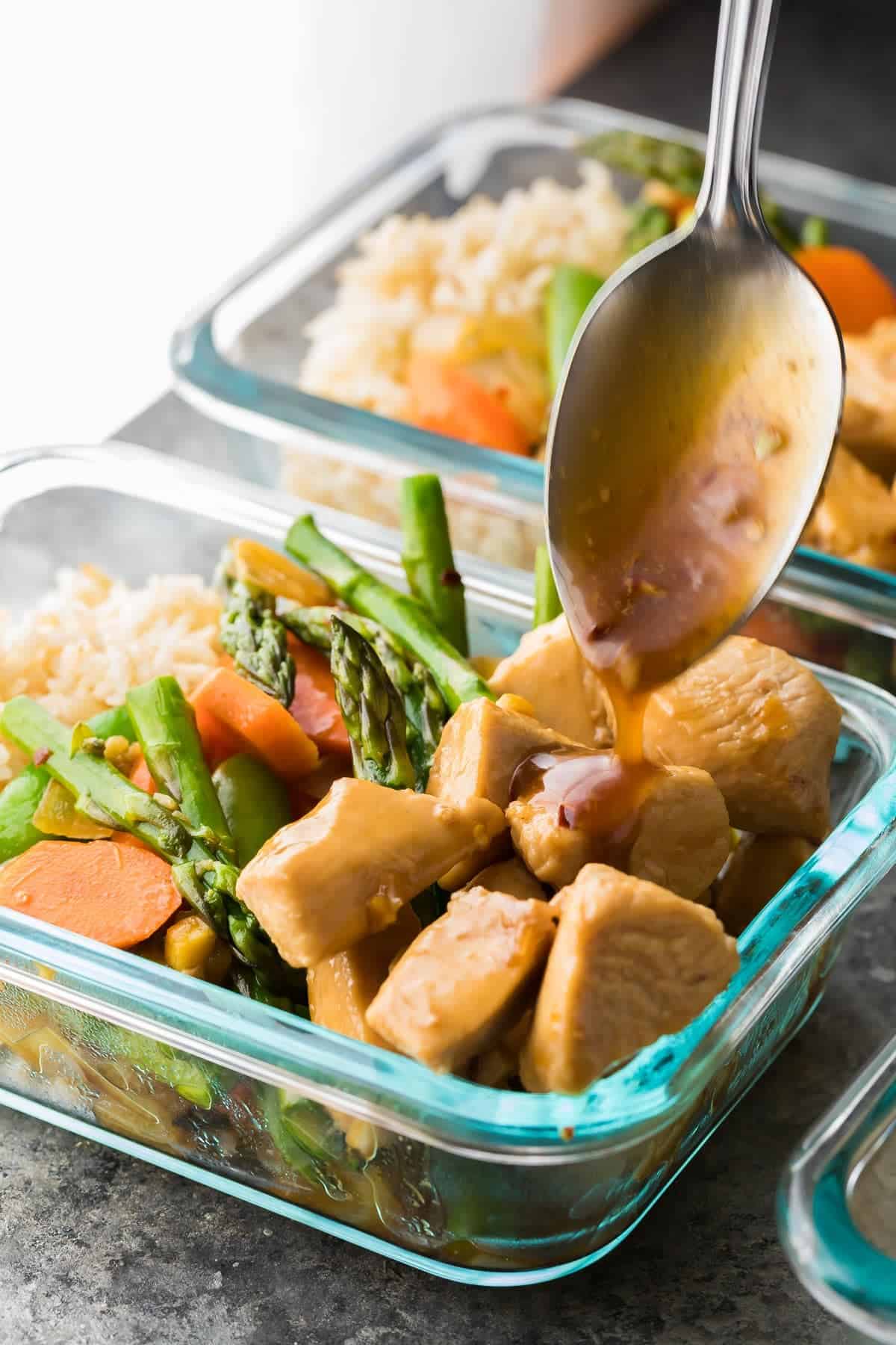 Spoon pouring sauce over Maple ginger chicken meal prep lunch bowls 