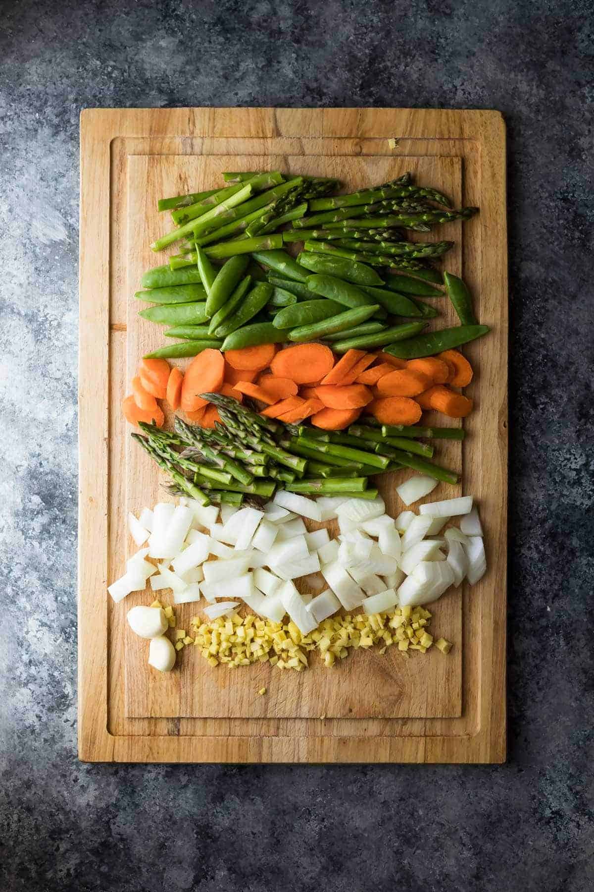 Overhead view of wood cutting board with a variety of raw chopped veggies