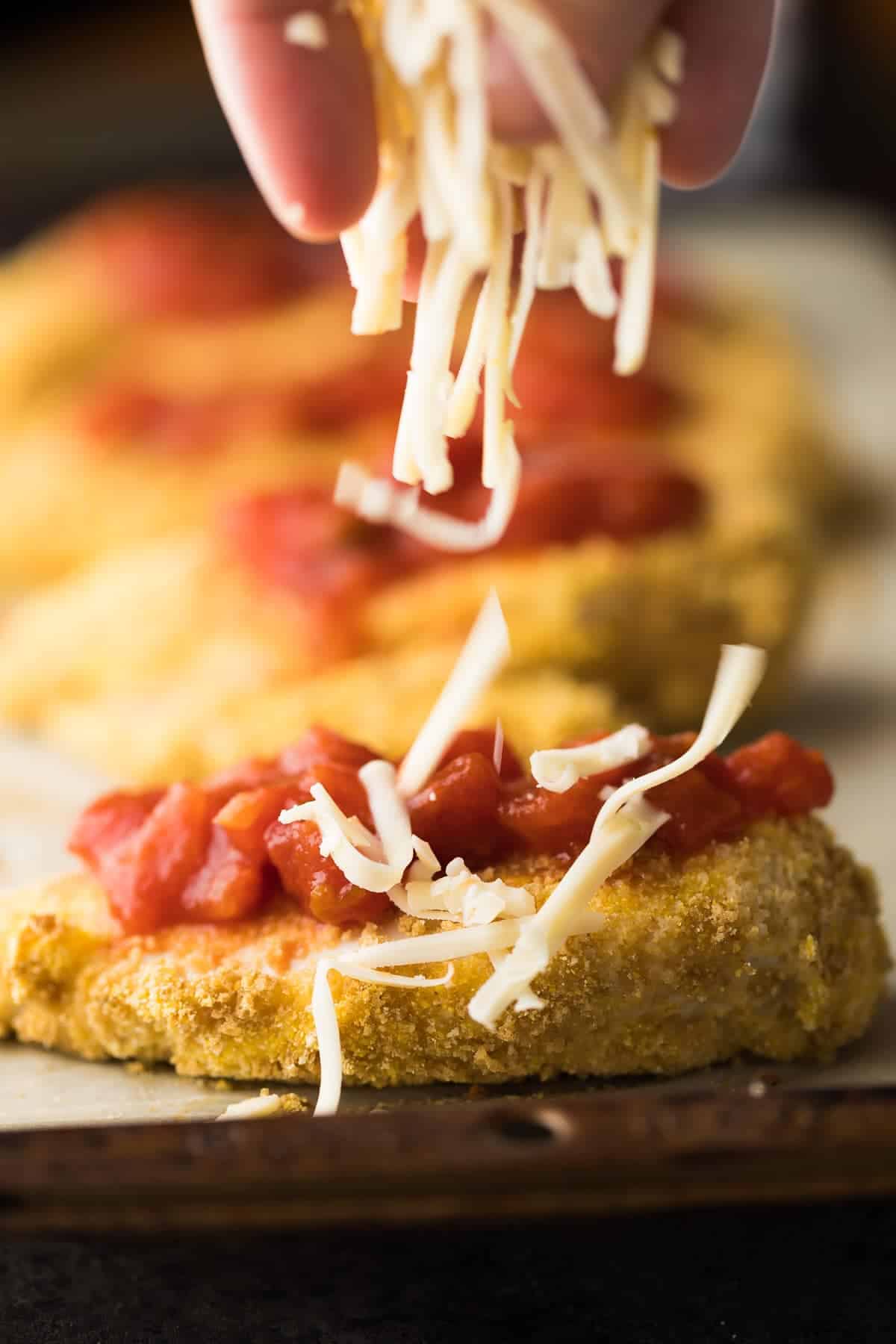 close up shot of a hand sprinkling shredded cheese onto chicken breast