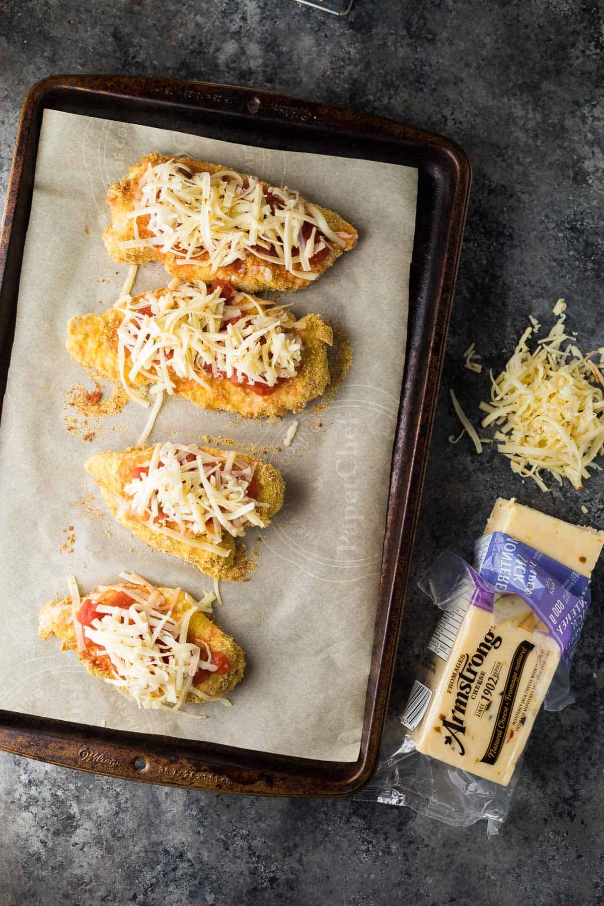 four breaded chicken breasts topped with shredded cheese on baking dish