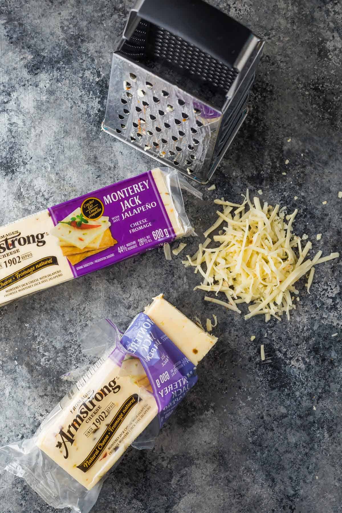 Two packages of Armstrong Monterey Jack Jalapeno cheese and a cheese grater