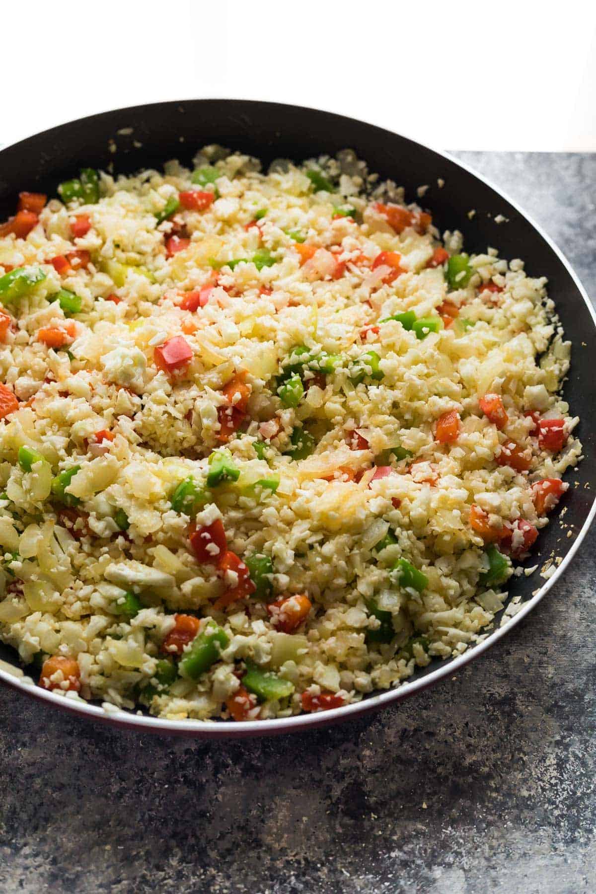 Large saute pan filled with all ingredients for cauliflower rice