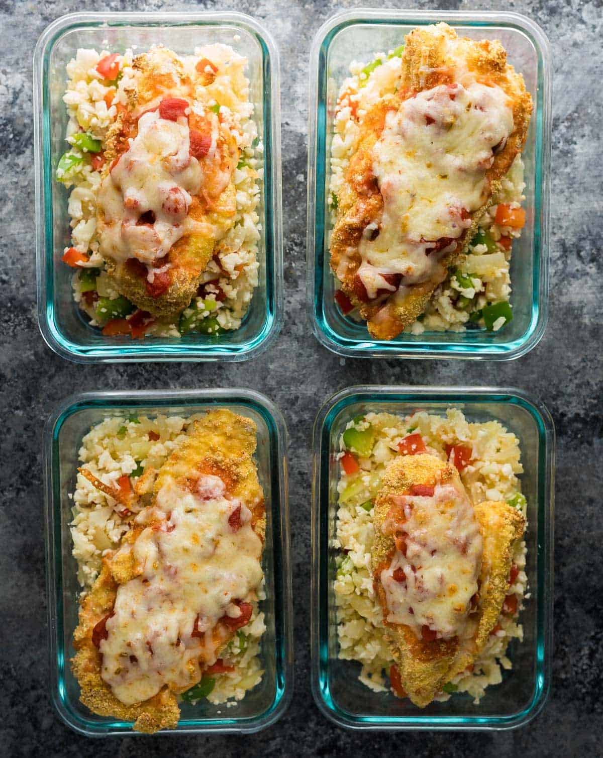 Overhead shot of four glass containers filled with Mexican chicken parm and cauliflower rice 