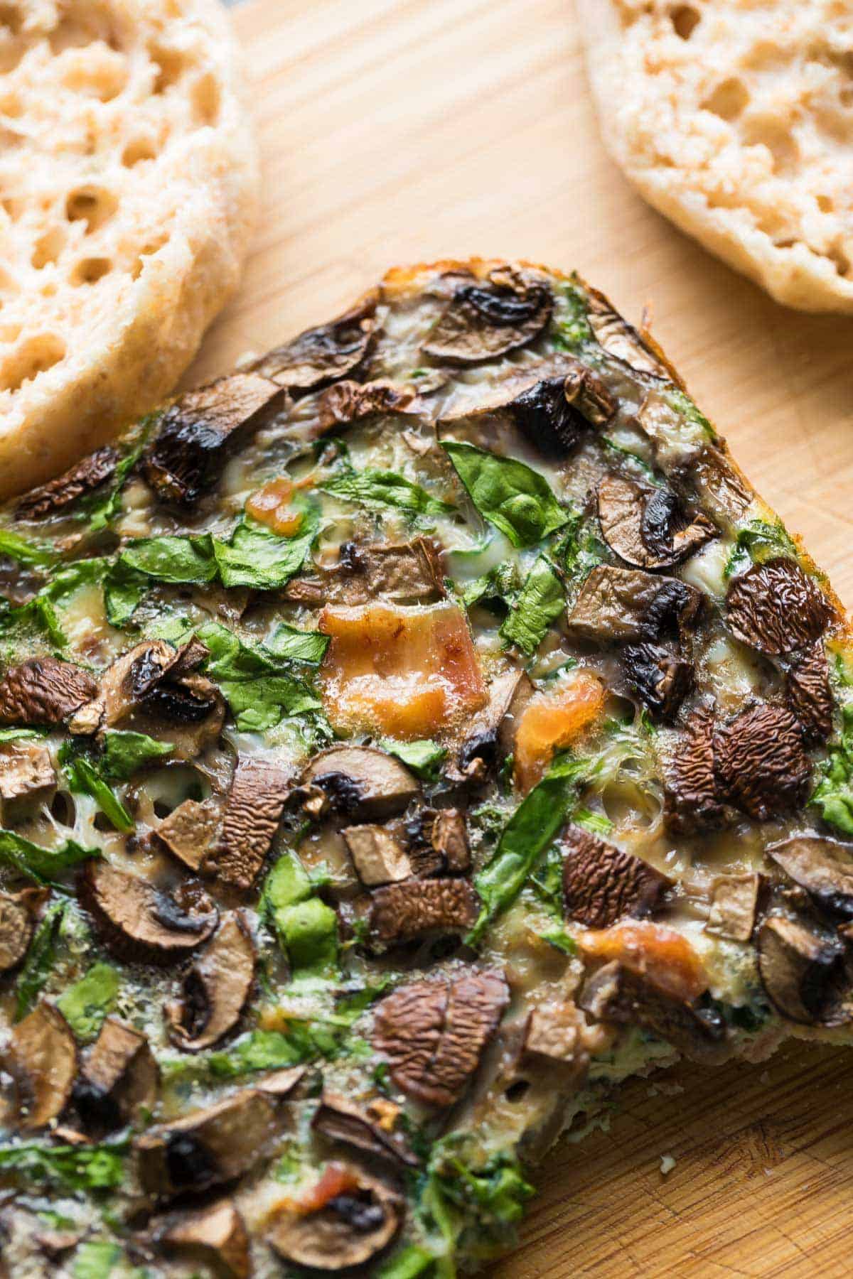 Mushroom bacon breakfast sandwich filling on cutting board with open english muffin behind it