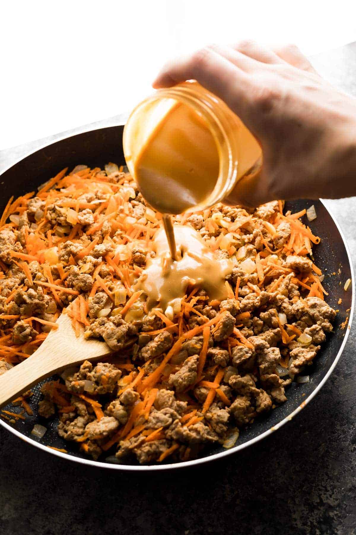 Pouring the peanut sauce into pan with ground turkey filling for lettuce wrap recipe