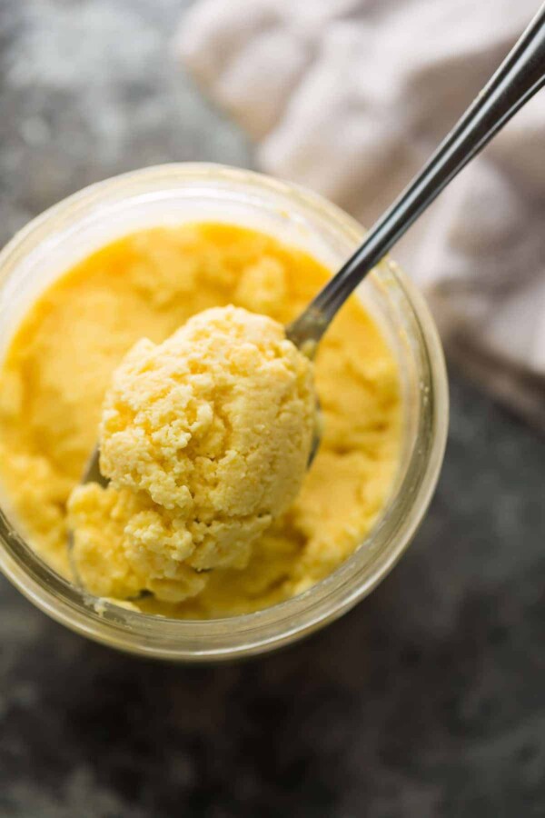 overhead shot of mango cheesecake frozen yogurt in glass jar with a spoon