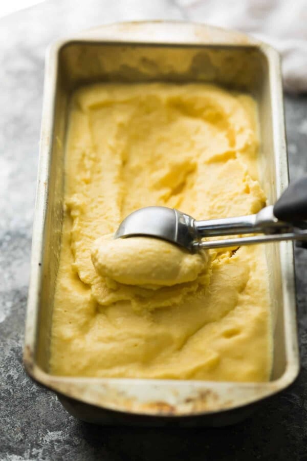 mango cheesecake frozen yogurt in pan with an icecream scoop scooping some out