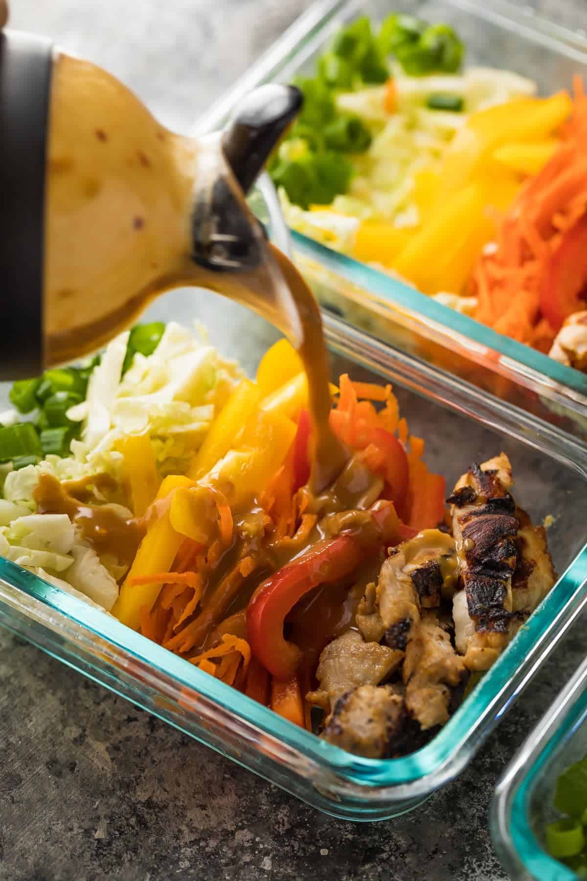 close up shot of dressing being poured over a satay chicken bowl