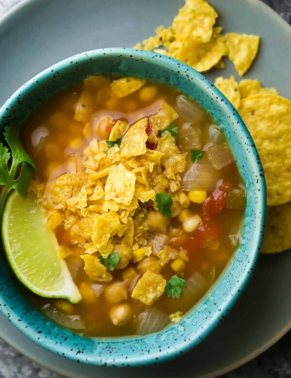 overhead shot of chickpea tortilla soup in blue bowl with lime wedge and tortilla chips
