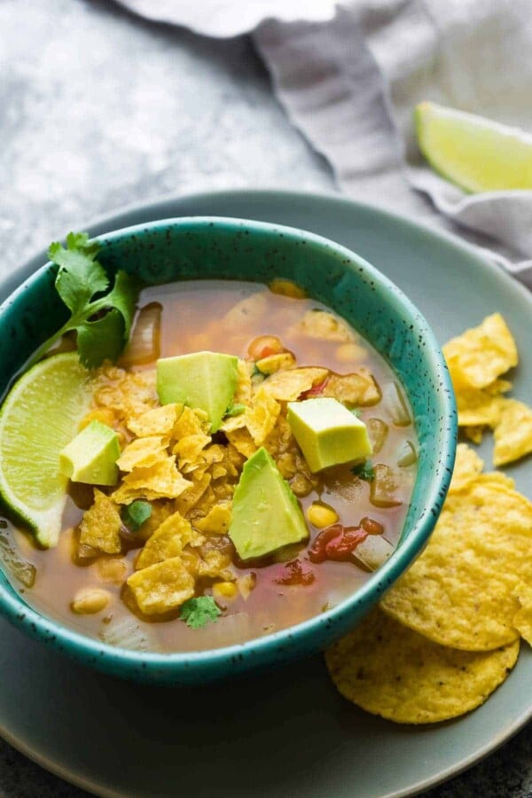 chickpea tortilla soup in blue bowl with tortilla chips, avocado slices and lime wedge