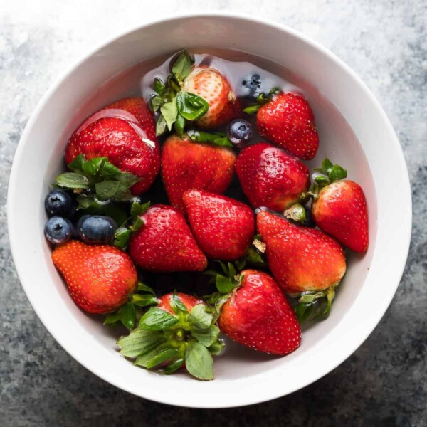 overhead shot of strawberries and blueberries being washed in a white bowl