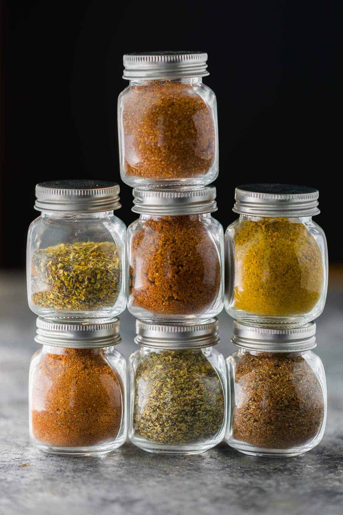 Seven glass jars in a stack filled with a variety of dry rub recipes