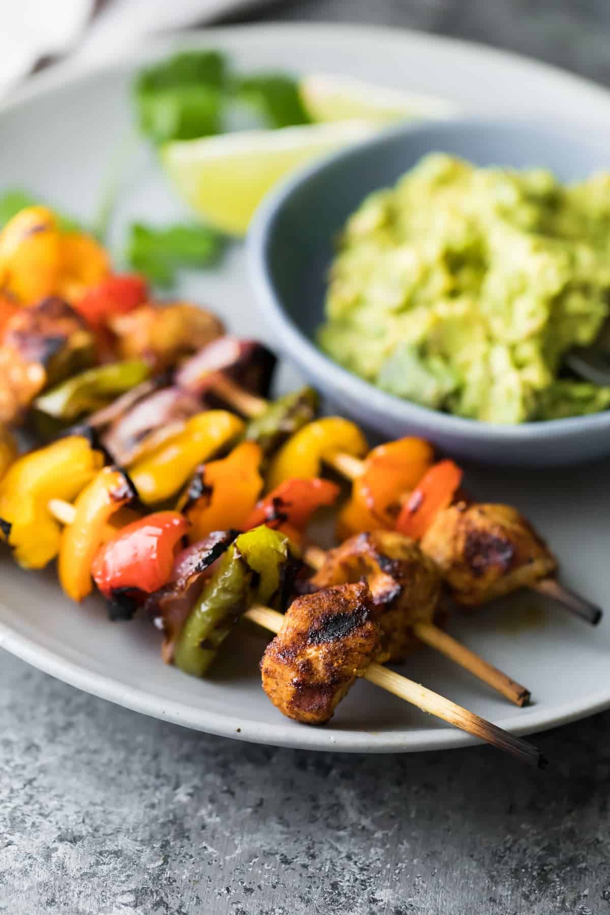 Three fajita chicken skewers on gray plate with side of guacamole