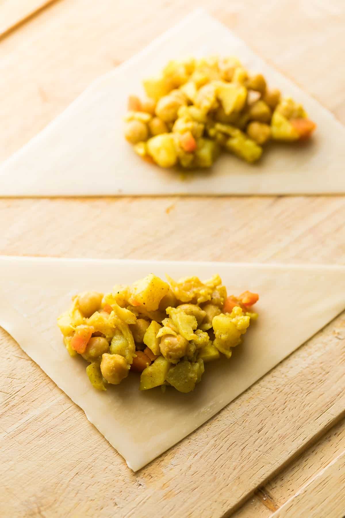 Two unwrapped samosa on a wooden table.