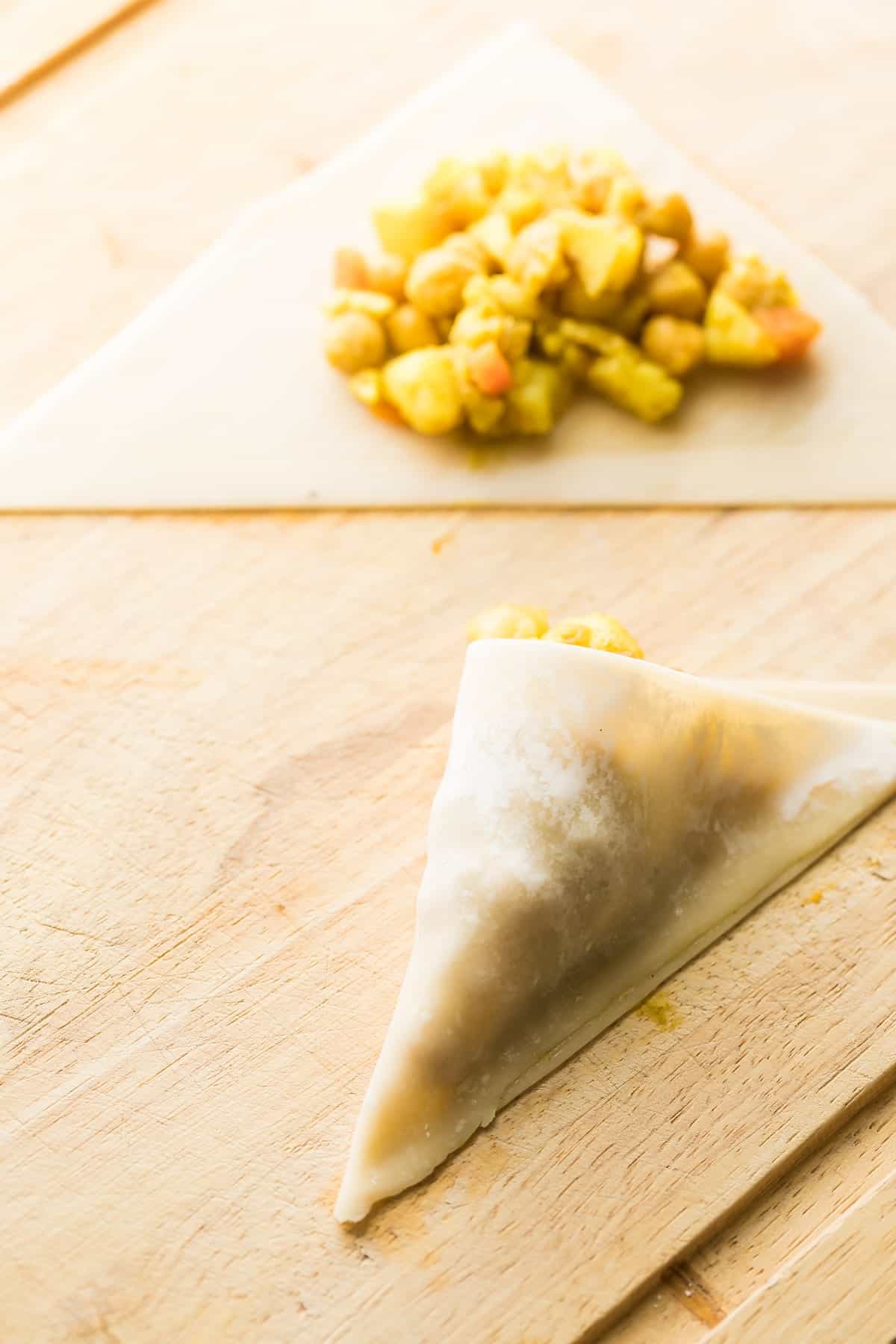 samosas being wrapped on a wooden cutting board
