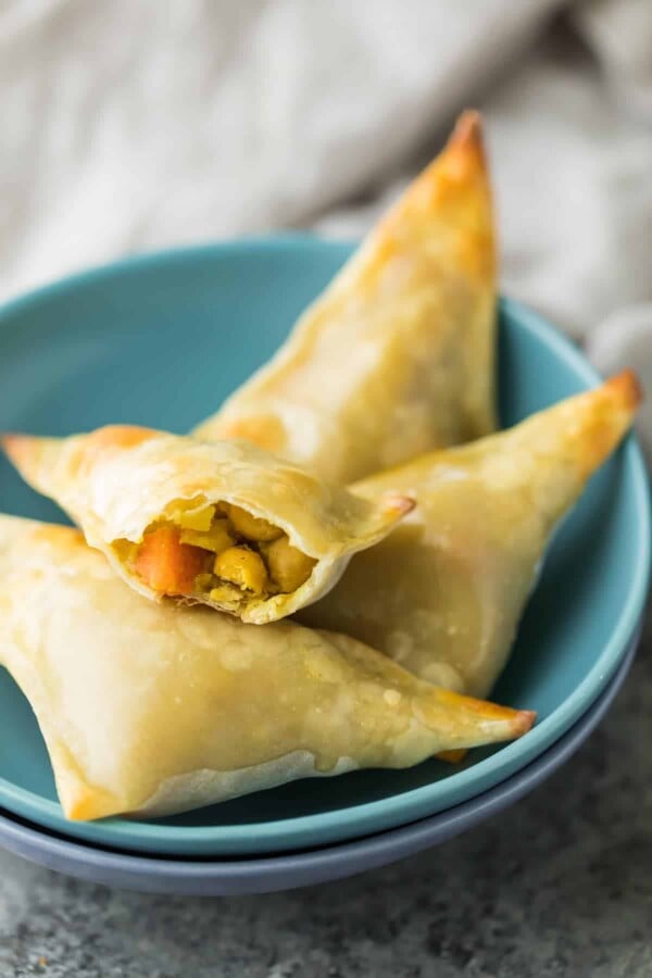 Four baked cauliflower chickpea samosas in stack of blue bowls