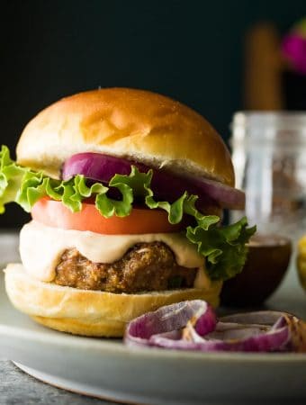 Side view of a Southwest Turkey Burger with guacamole and red onion on a plate with dish of sauce in the background