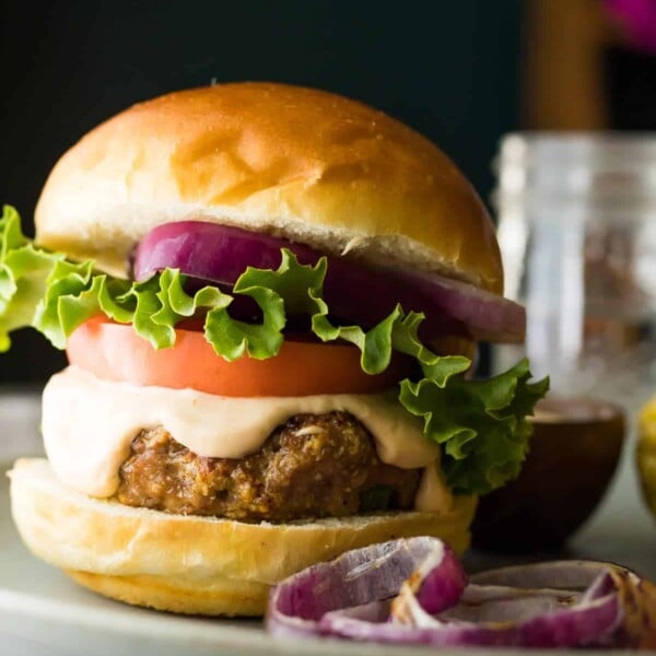 Side view of a Southwest Turkey Burger with guacamole and red onion on a plate with dish of sauce in the background