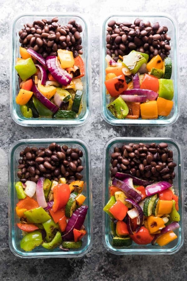 Four grilled vegetable and black bean meal prep bowls in glass storage containers